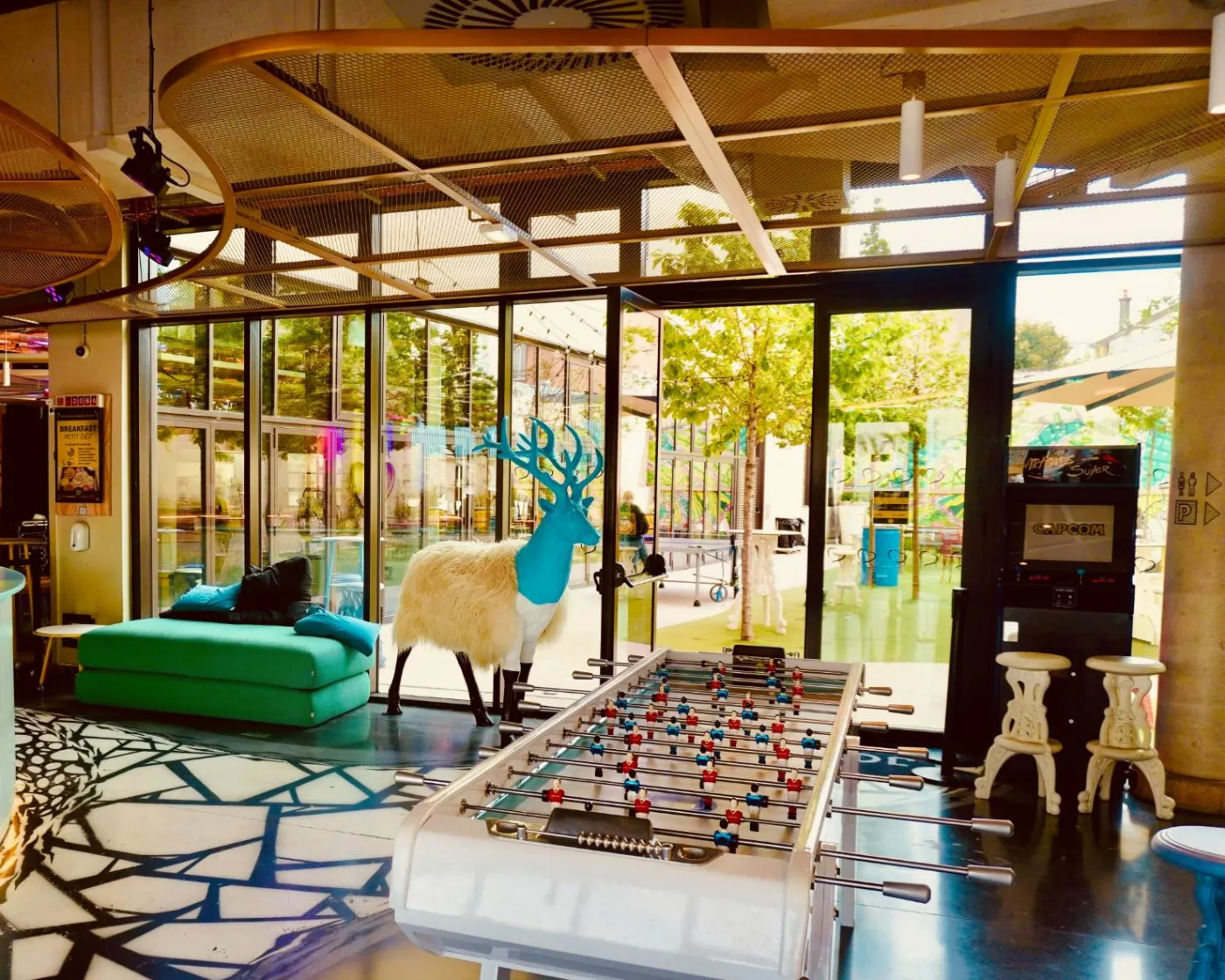 A hostel common room with a foosball table, arcade machine and garden terrace