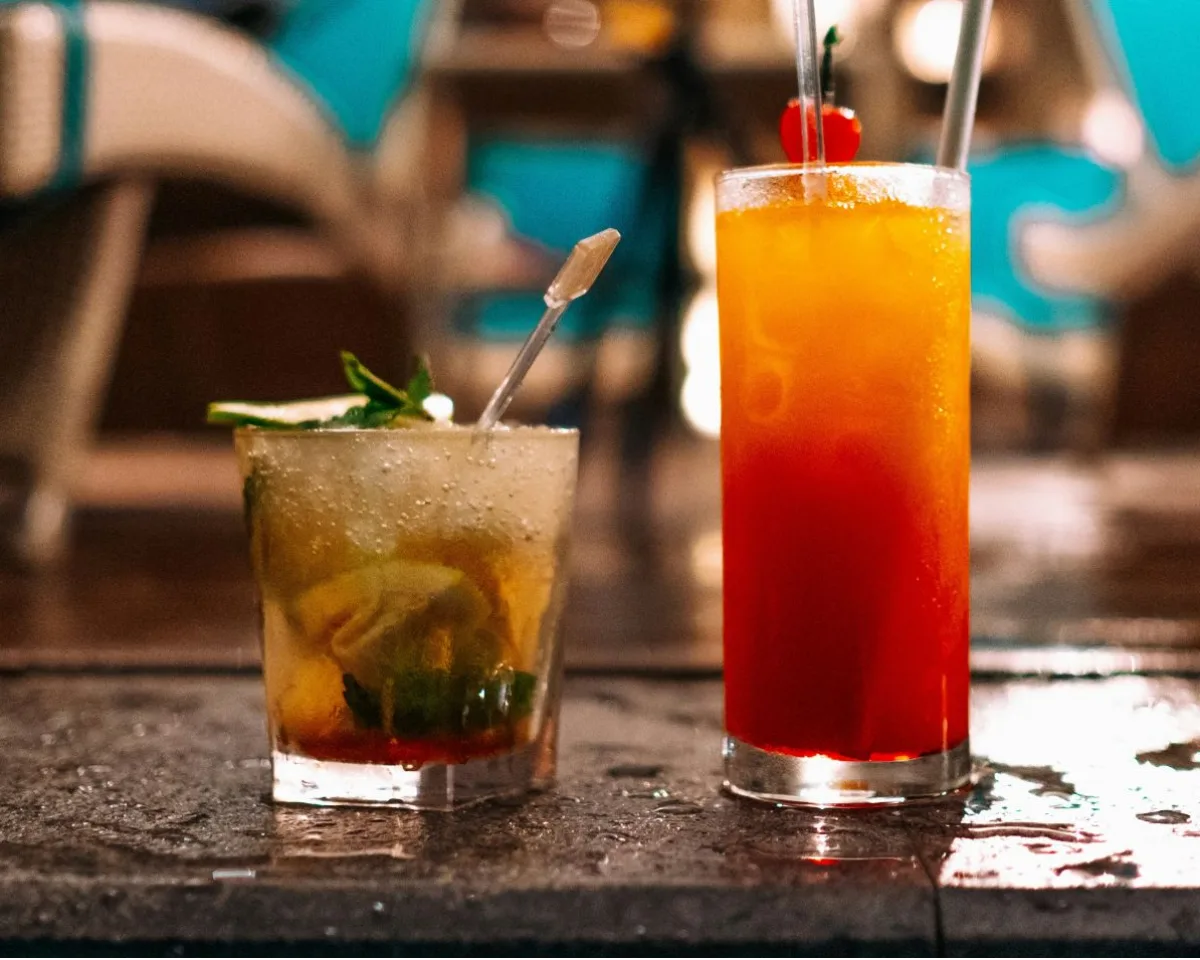 Two cocktails on a wet bar top beside a pool deck with turquoise sunloungers